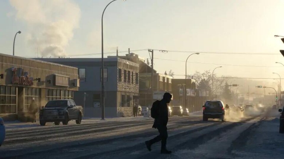 une personne tranverse la rue, sous la neige.