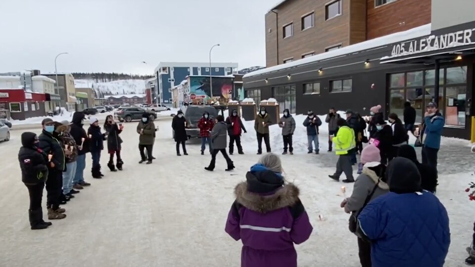 Des gens rassemblés en cercle devant un édifice en hiver.