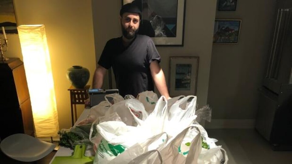 Yusuf Celik devant une table avec des sacs de course.