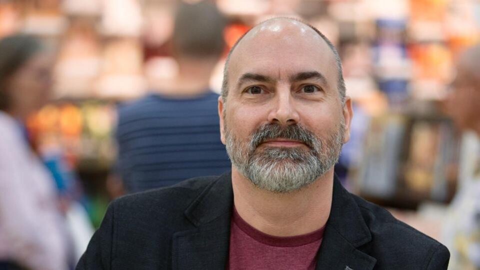 L’auteur Yvan Godbout photographié lors d’un salon du livre. On aperçoit, à l’avant-plan, une copie de son roman «Les Yeux jaunes».
