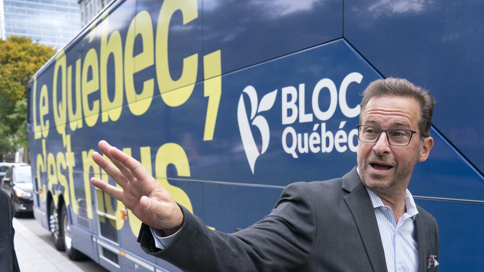 Yves-François Blanchet sourit et tend la main, devant l'autobus du Bloc québécois.