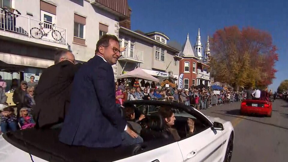 Yves-François Blanchet assis à l'arrière d'une voiture décapotable que des passants regardent défiler.