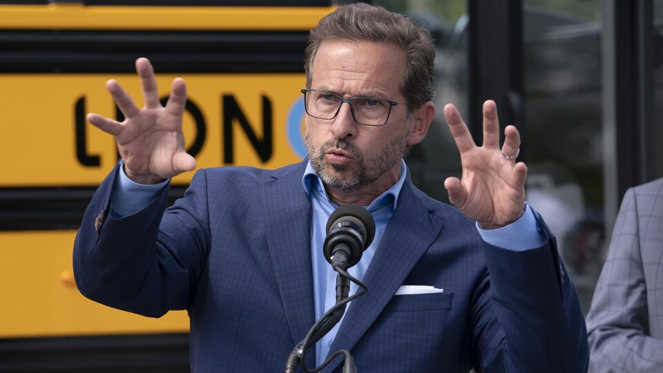 L'air sérieux, Yves-François Blanchet lève les deux mains à hauteur de son visage. Il s'adresse aux médias devant un autobus scolaire.