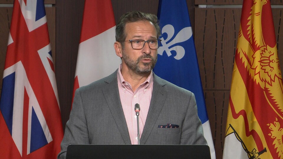 Derrière un lutrin, Yves-François Blanchet s'adresse aux journalistes avec à l'arrière-plan des drapeaux du Canada et des provinces.