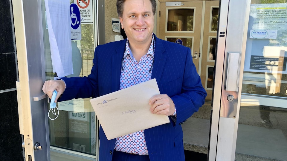 Yves Montigny, avec un veston bleu, tient son dossier de candidature.