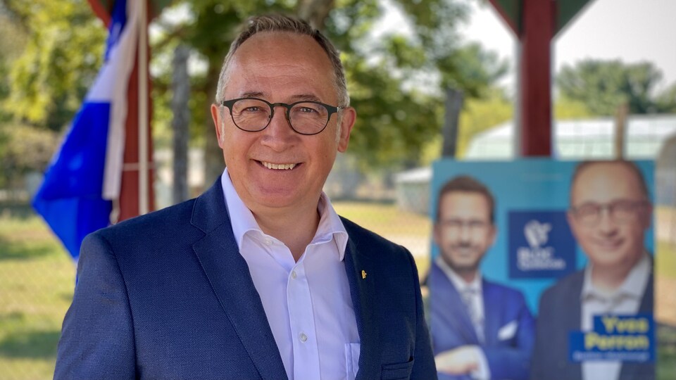 Yves Perron, candidat du Bloc québécois, prend la pose devant une pancarte électorale.