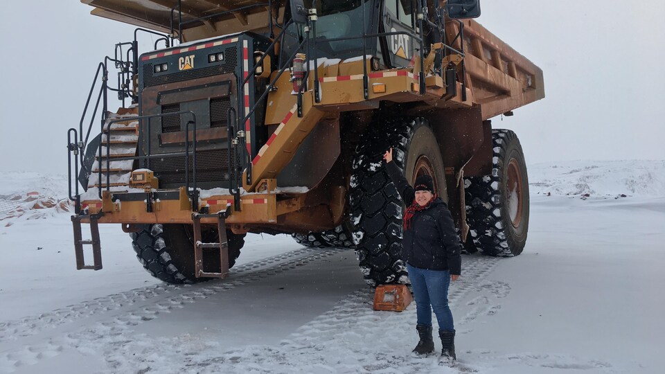 La femme au pied d'un énorme camion qui parcourt les mines.