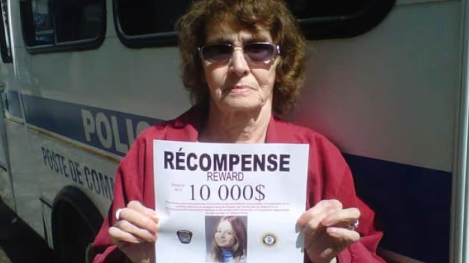 Une femme tient l'affiche offrant une récompense.