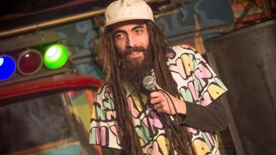 L'homme barbu porte une casquette et tient un micro.