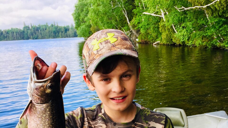 Un enfant tient une truite arc-en-ciel qu'il vient de pêcher.