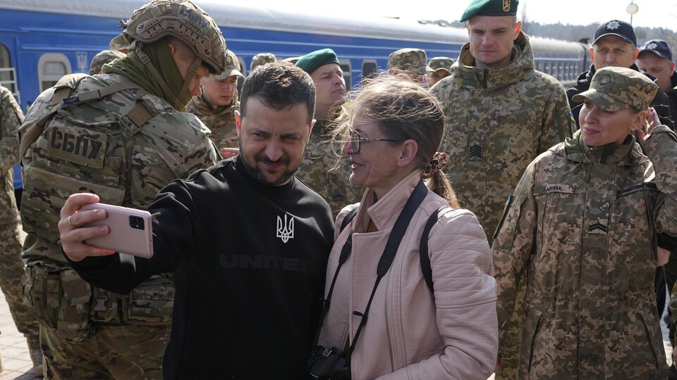 Un homme prend un égoportrait avec une femme, tous deux entourés de militaires.
