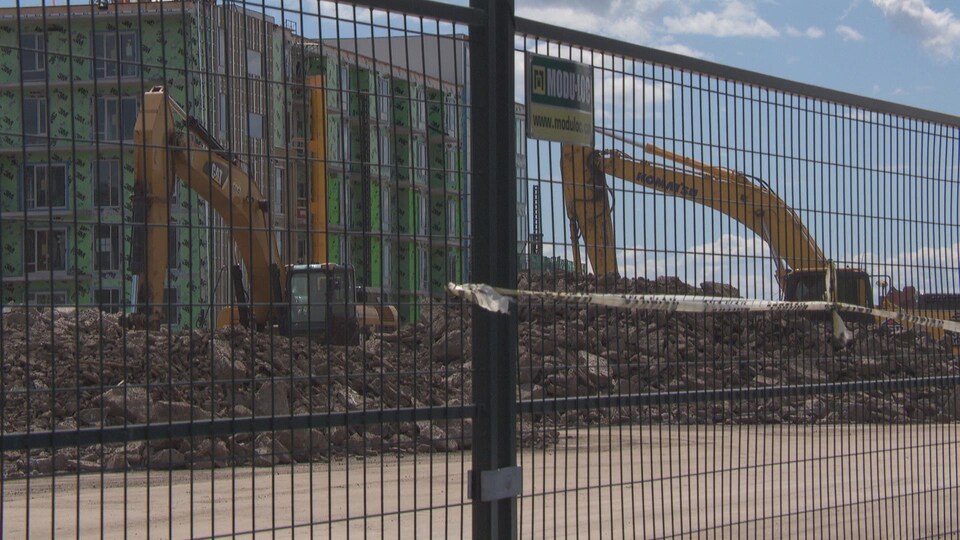 Deux grues s'affairent à retirer des roches et du sol autour de l'immeuble en construction.