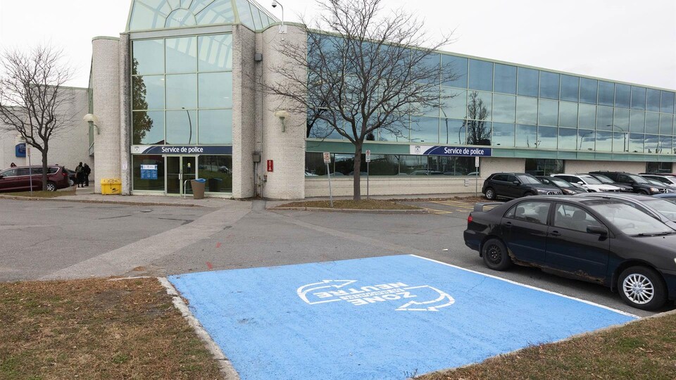 Un grand carré bleu a été peint au sol. Dans celui-ci, on peut lire : Zone neutre. En arrière plan, on voit la porte du poste de police. 