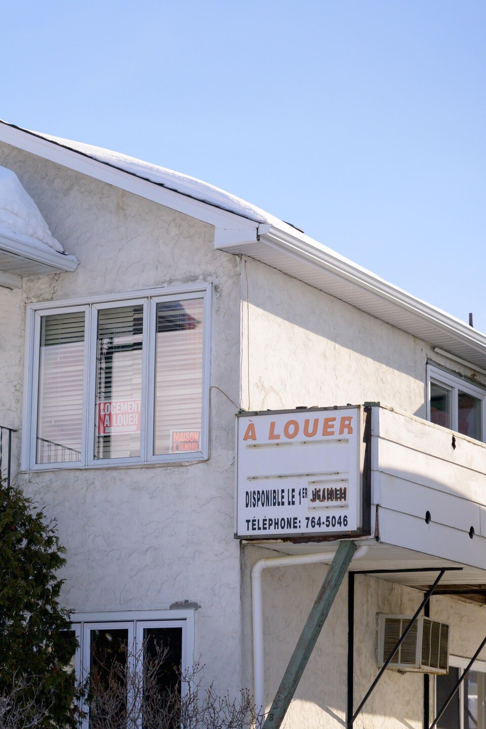 Un panneau «À louer» est affiché sur le balcon d'une maison enneigée.