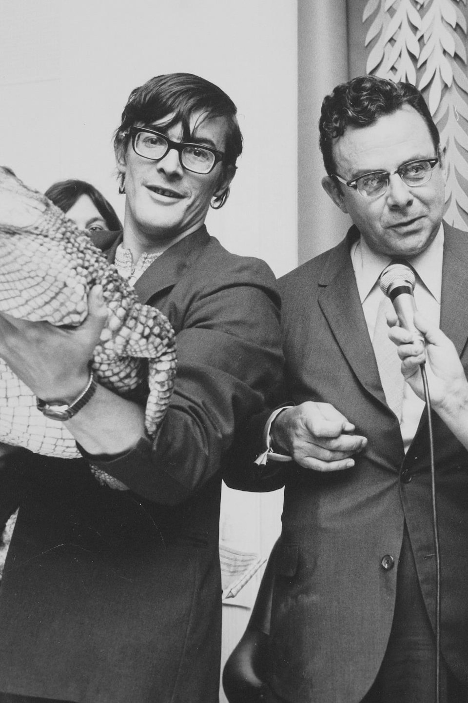 Lise Payette rit tout en tendant le micro à Gilles Charbonneau. À leurs côtés, un vétérinaire tient un crocodile dans ses bras.
