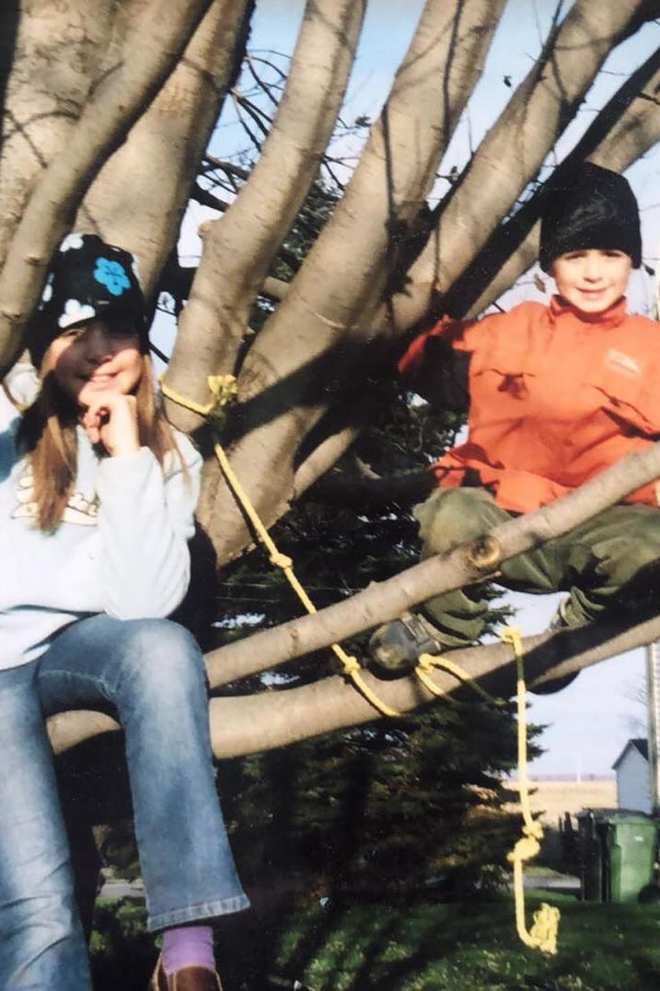 Ariane et Thomas-Louis sont assis dans les branches d'un grand arbre. À l'arrière-plan se dessine la maison familiale.