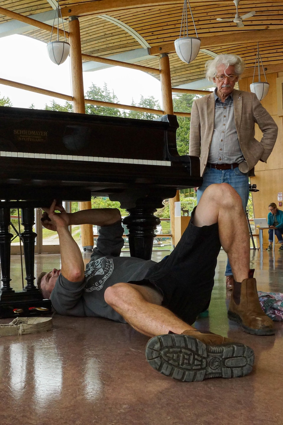 Un homme allongé sous un piano fait des ajustements.