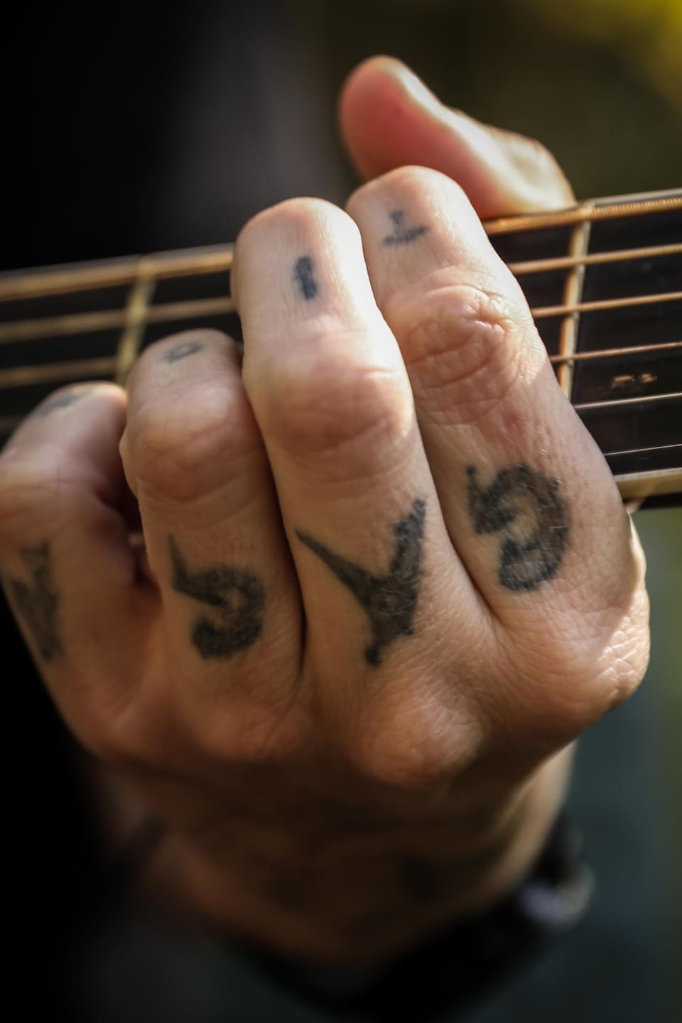 Une main tatouée qui tient un manche de guitare