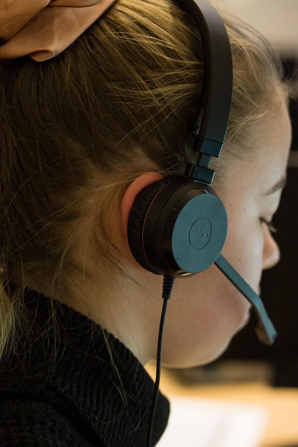 Une jeune femme avec un casque d'écoute regarde son écran.