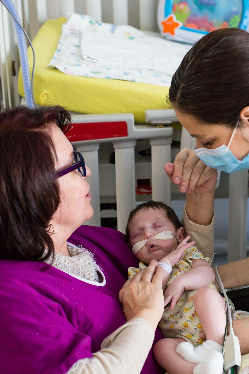 Une infirmière dépose un bébé prématuré dans les bras de la bénévole Louise Lafond.