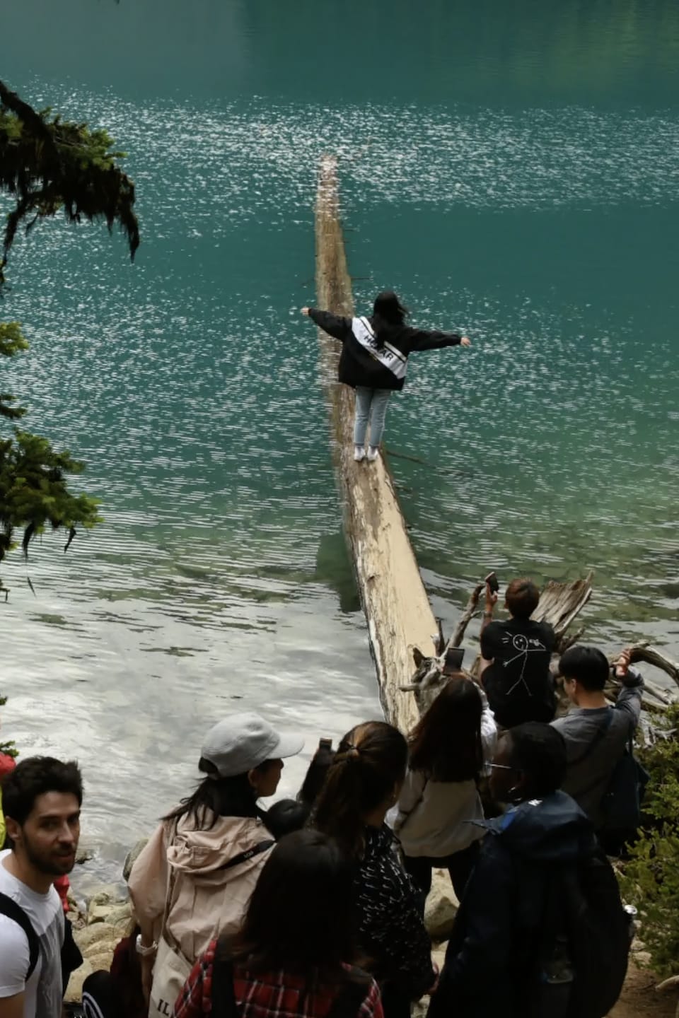 Une touriste s'installe sur un tronc à demi-submergé dans un lac du parc britanno-colombien Joffre Lakes afin de prendre une photo pour Instagram. Plusieurs personnes attendent leur tour pour faire de même.