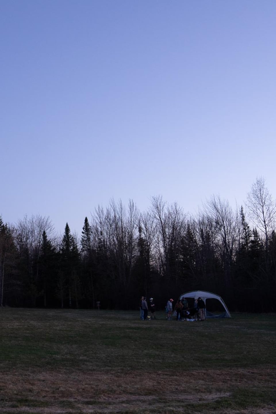 Quelques personnes regroupées autour d'une tente à la brunante à la base de plein air André-Nadeau à Sherbrooke. 