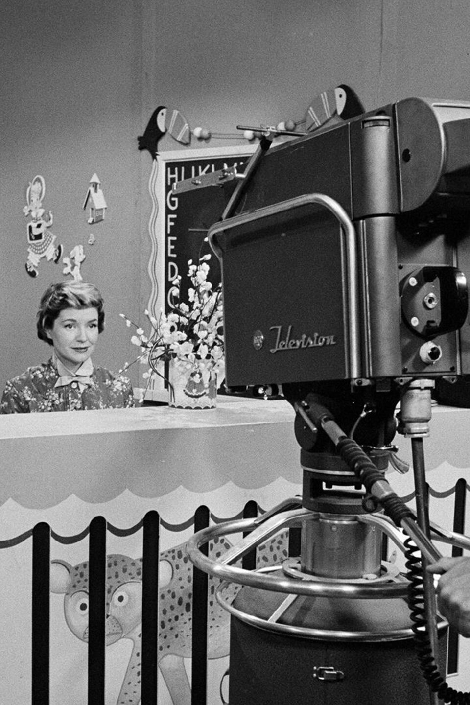 Un caméraman filme l'animatrice Lise Roy, assise derrière un comptoir dans le studio de l'émission jeunesse.