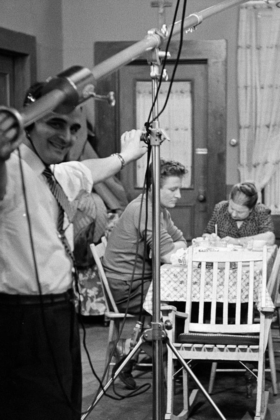 Vue d'ensemble du plateau de tournage avec le preneur de son et la caméra filmant une scène dans la cuisine des Plouffe avec les comédiens Pierre Valcourt, Amanda Alarie et Paul Guèvremont.