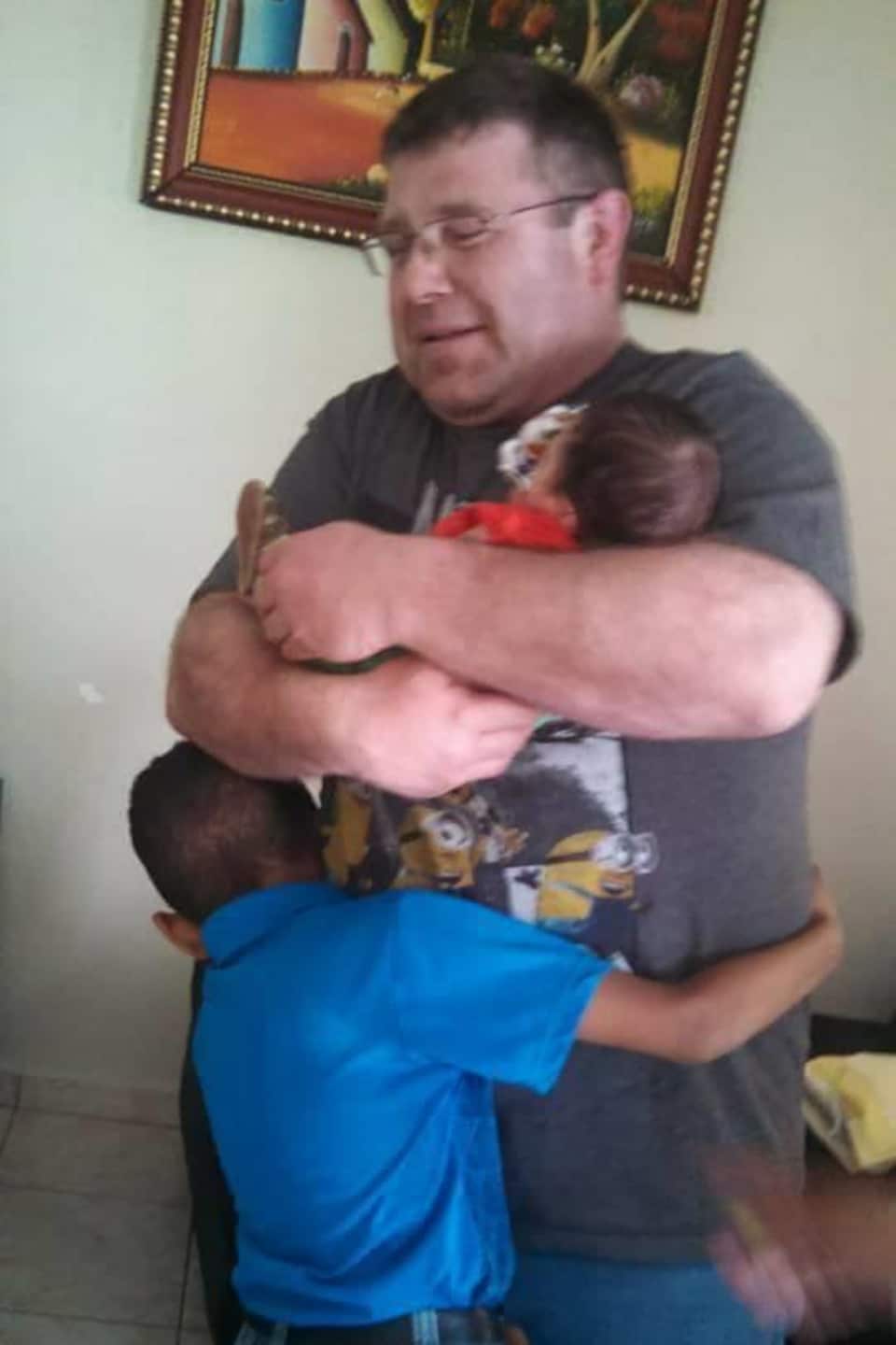 Danny held a young baby in his arms as a boy hugged him.