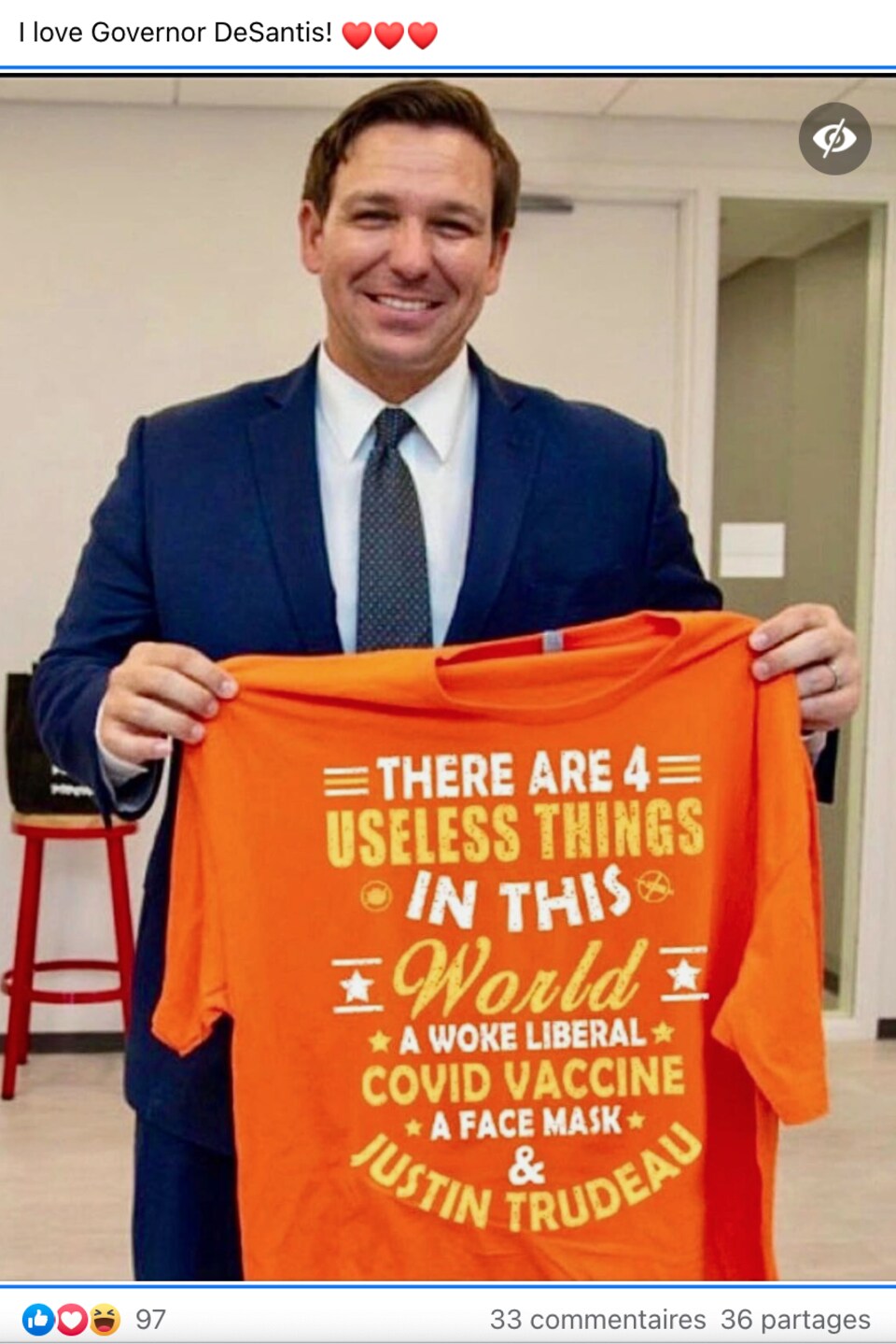 Le gouverneur de la Floride tient un t-shirt orange. Il s'agit d'une image truquée. On lit, en anglais, « Il y a quatre choses inutiles dans ce monde : un libéral woke, le vaccin contre la COVID, le masque et Justin Trudeau. »