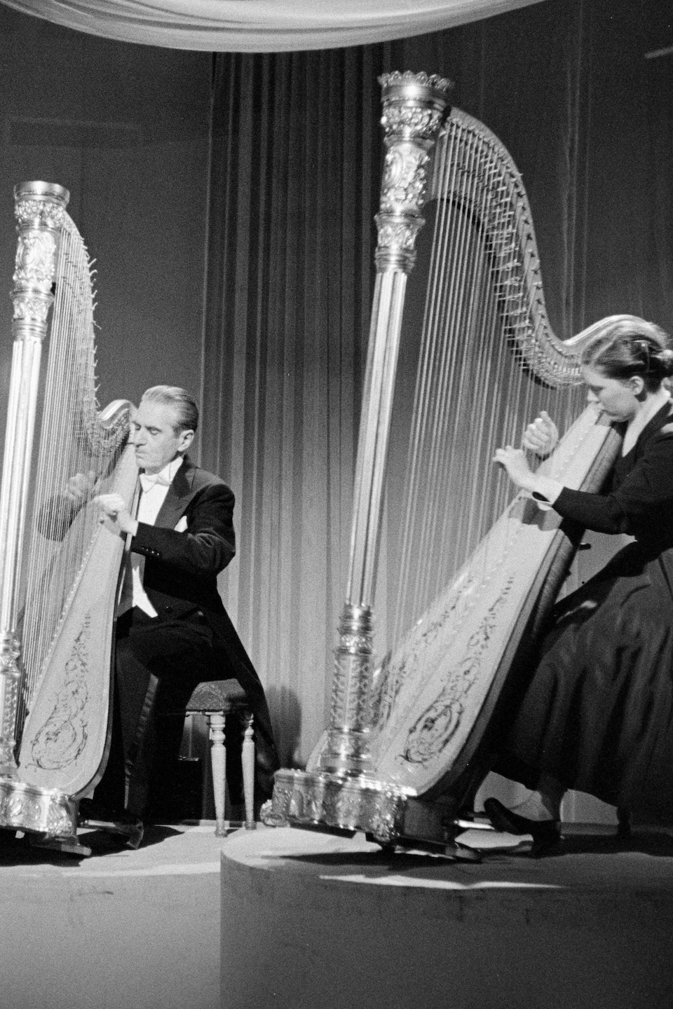 Dorothy Weldon, Marcel Grandjany et Marie Iösch assis, jouant de la harpe, chacun sur sa plateforme dans un studio de télévision décoré de voilages.