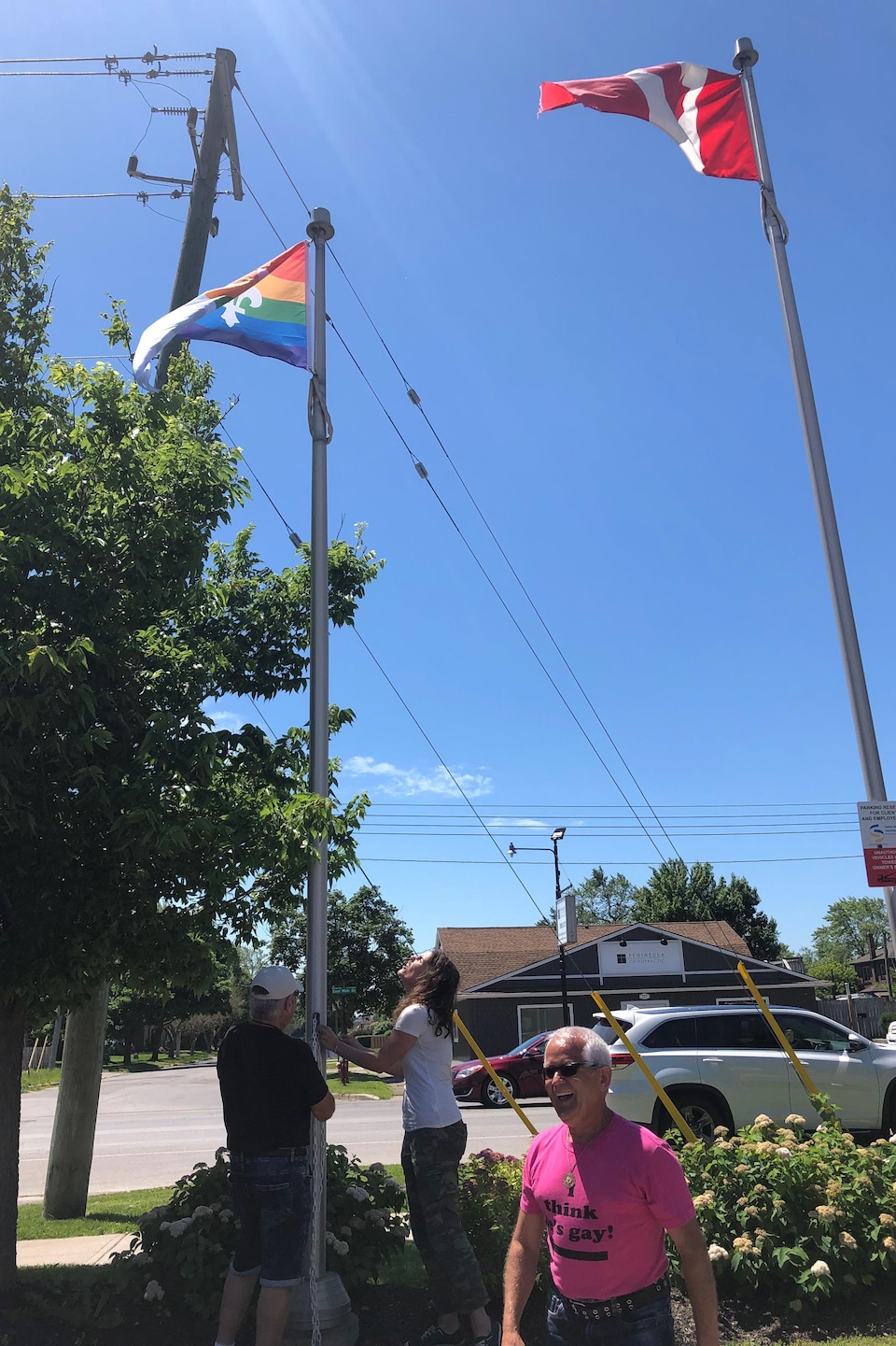 Trois personnes souriantes s'assurent que le drapeau est bien dans les airs. 