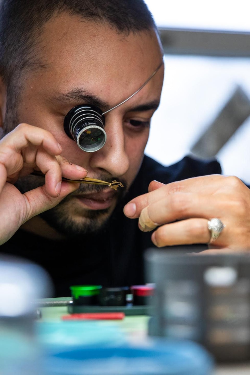 Un homme avec une loupe sur l'œil observe une petite pièce. 