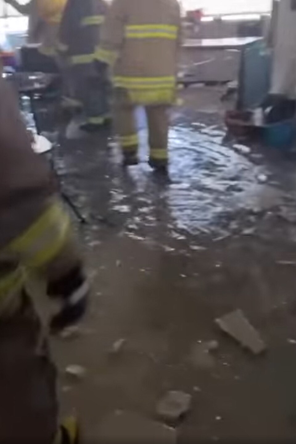 Des pompiers marchent sur un plancher inondé.