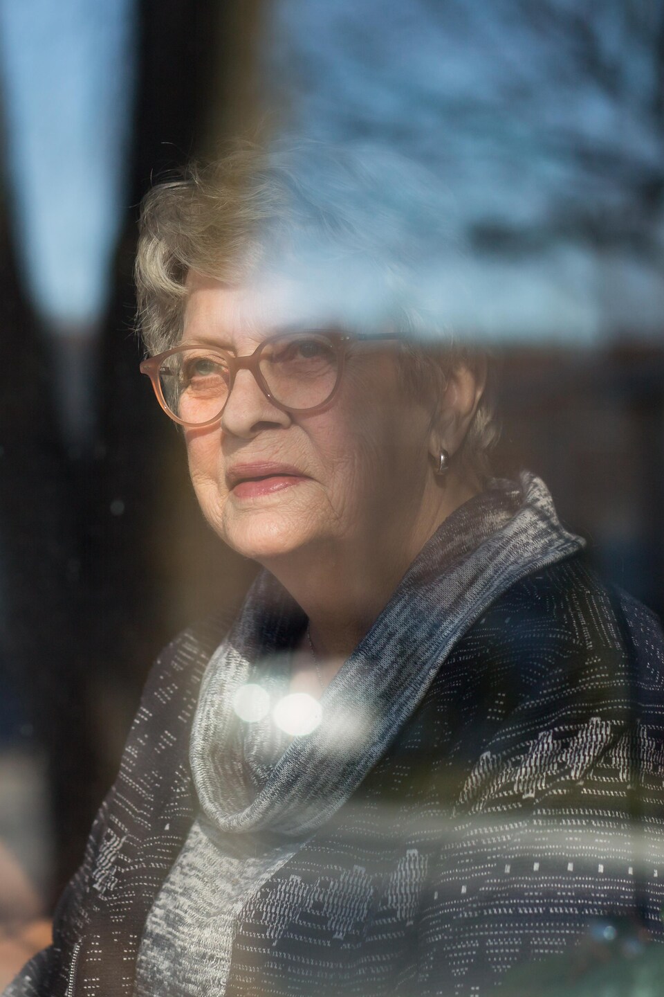 Ellen Schryburt pose derrière la vitre de son salon.