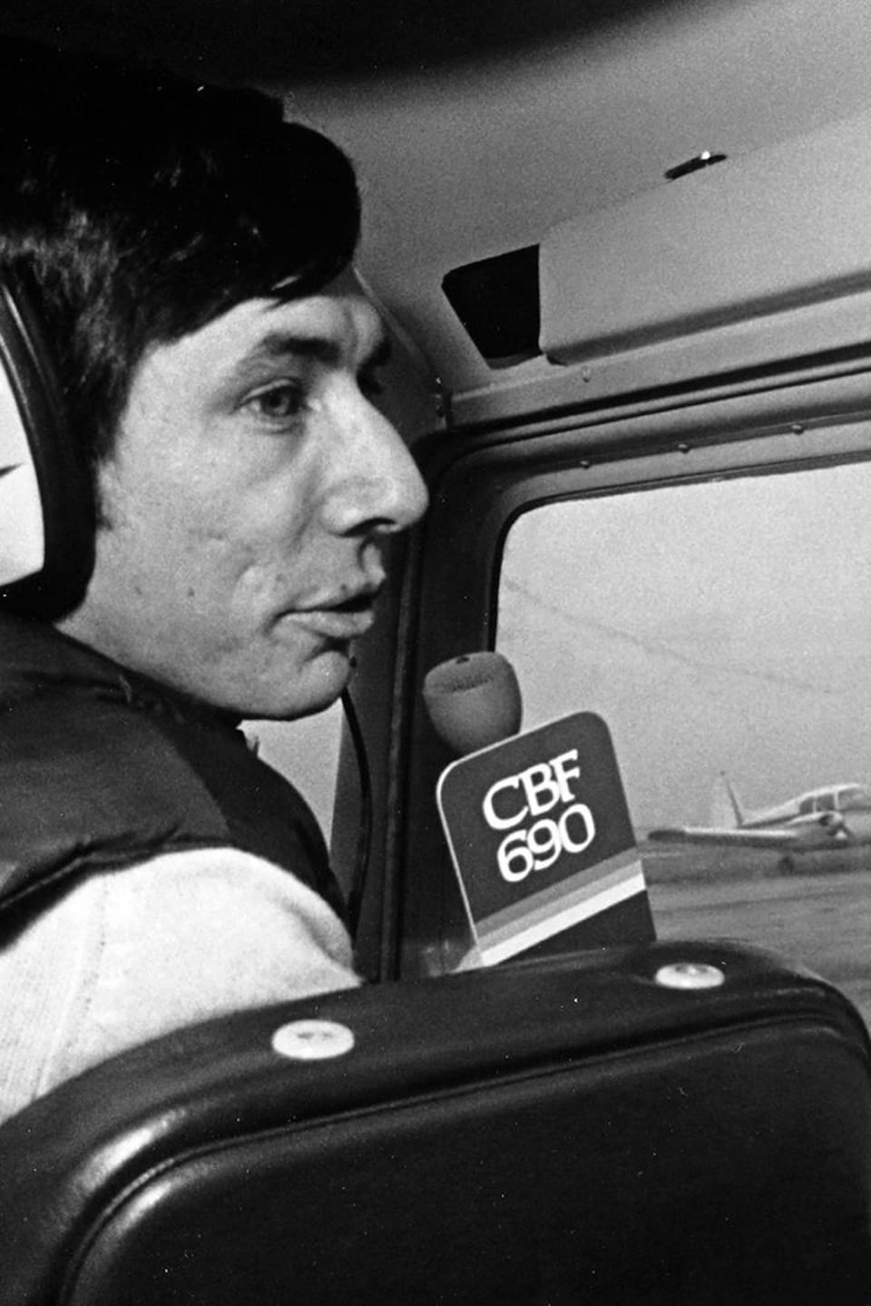 Roger Laroche à bord d'un petit avion, micro de CBF à la main.
