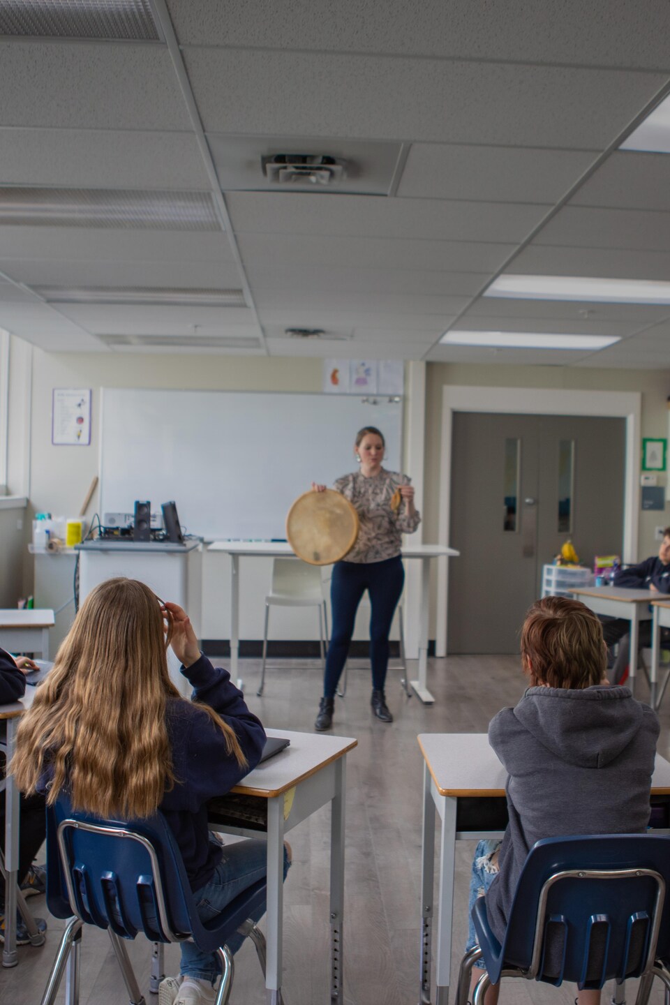 Bonnie Lépine est devant une classe de plusieurs élèves et leur montre un tambour traditionnel autochtone. 