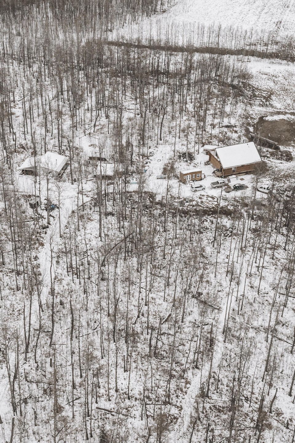 Une cabine en bois rond, avec d'autres constructions et des voitures, au milieu de la forêt, le sol couvert de neige, en novembre 2023, près de Cremona, en Alberta.