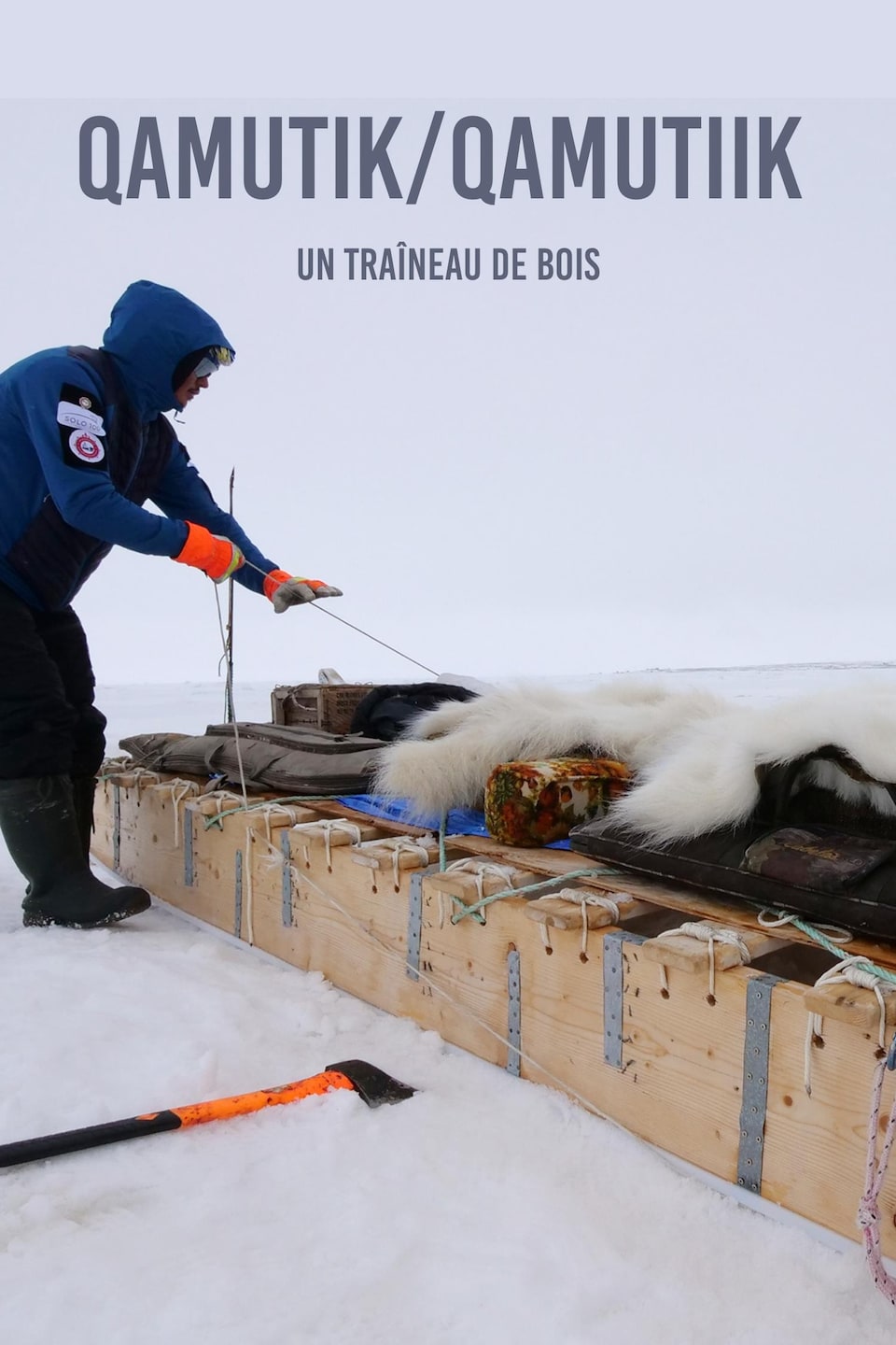 Le mot en inuktitut qamutik et sa traduction  un traîneau de bois écrit sur une photo de Devon Manik en train d’atteler son traîneau avec son équipement, au mois de juin à Resolute Bay, dans le nord du Nunavut.