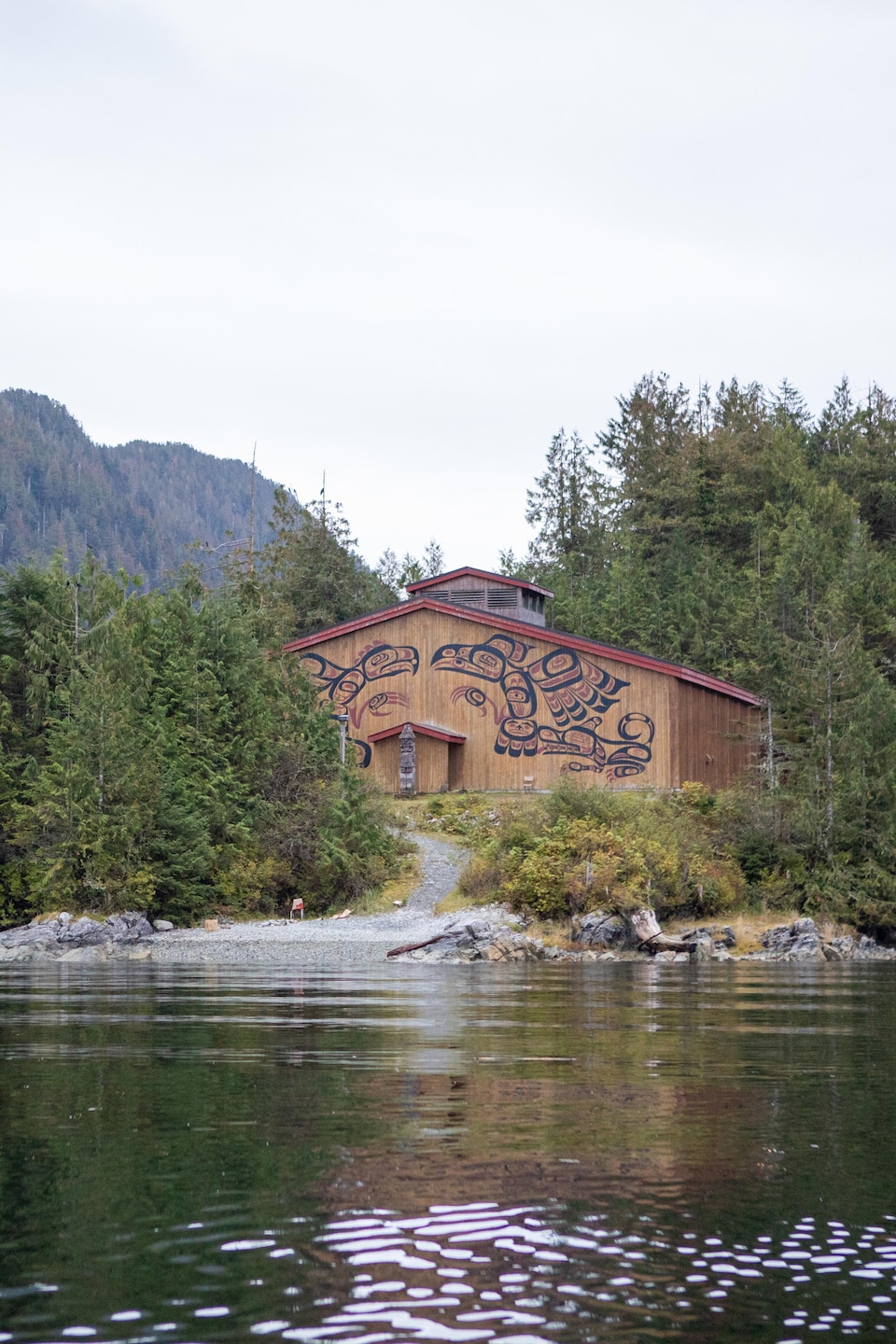 Une maison en bois avec des peintures traditionnelles autochtones, au bord de la rivière, dans la forêt, près de Klemtu, en Colombie-Britannique, en octobre 2023.