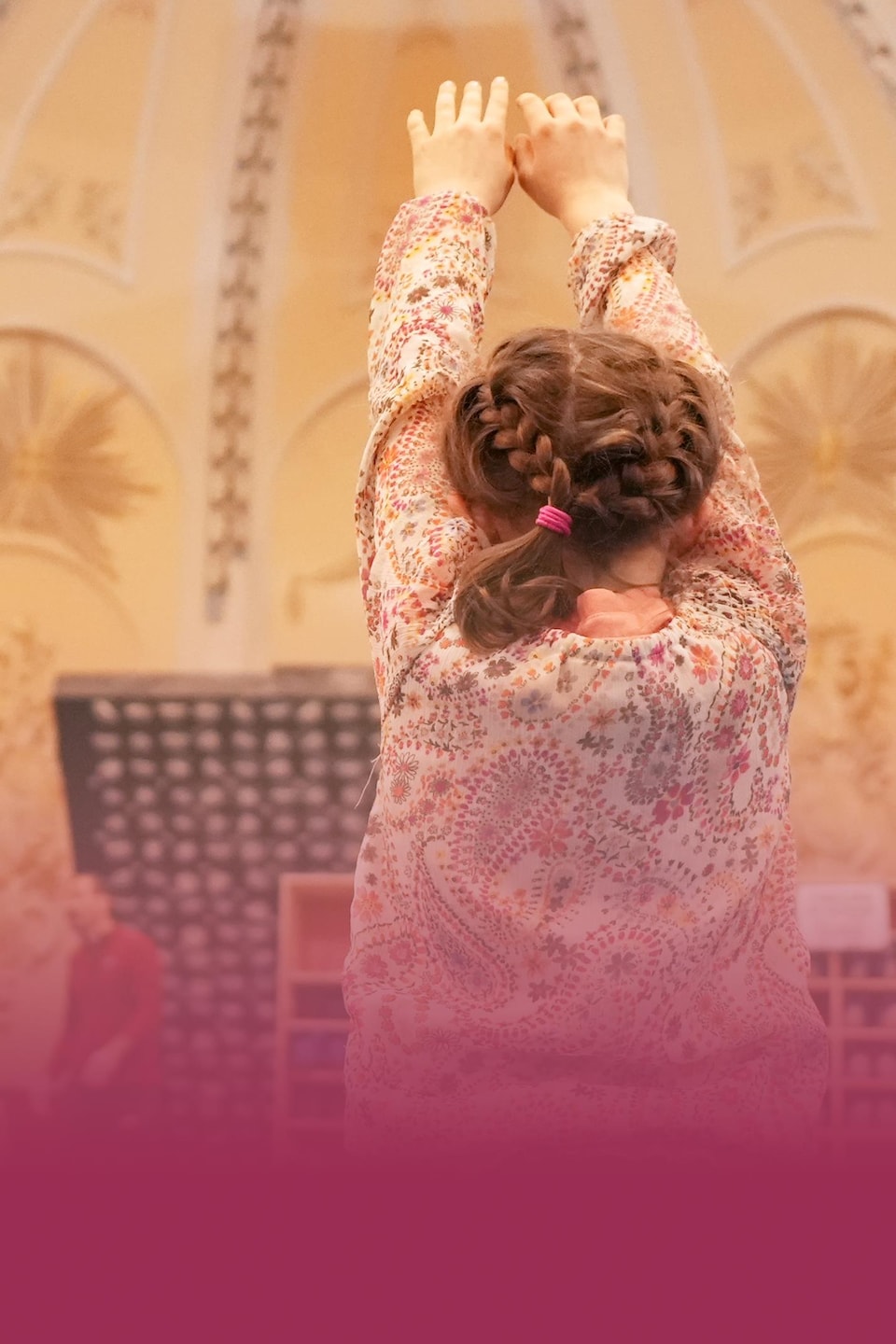 Une petite fille, de dos, se prépare à faire une culbute au sol. En arrière d'elle, l'on distingue le plafond orné de l'église et des murs d'escalade.