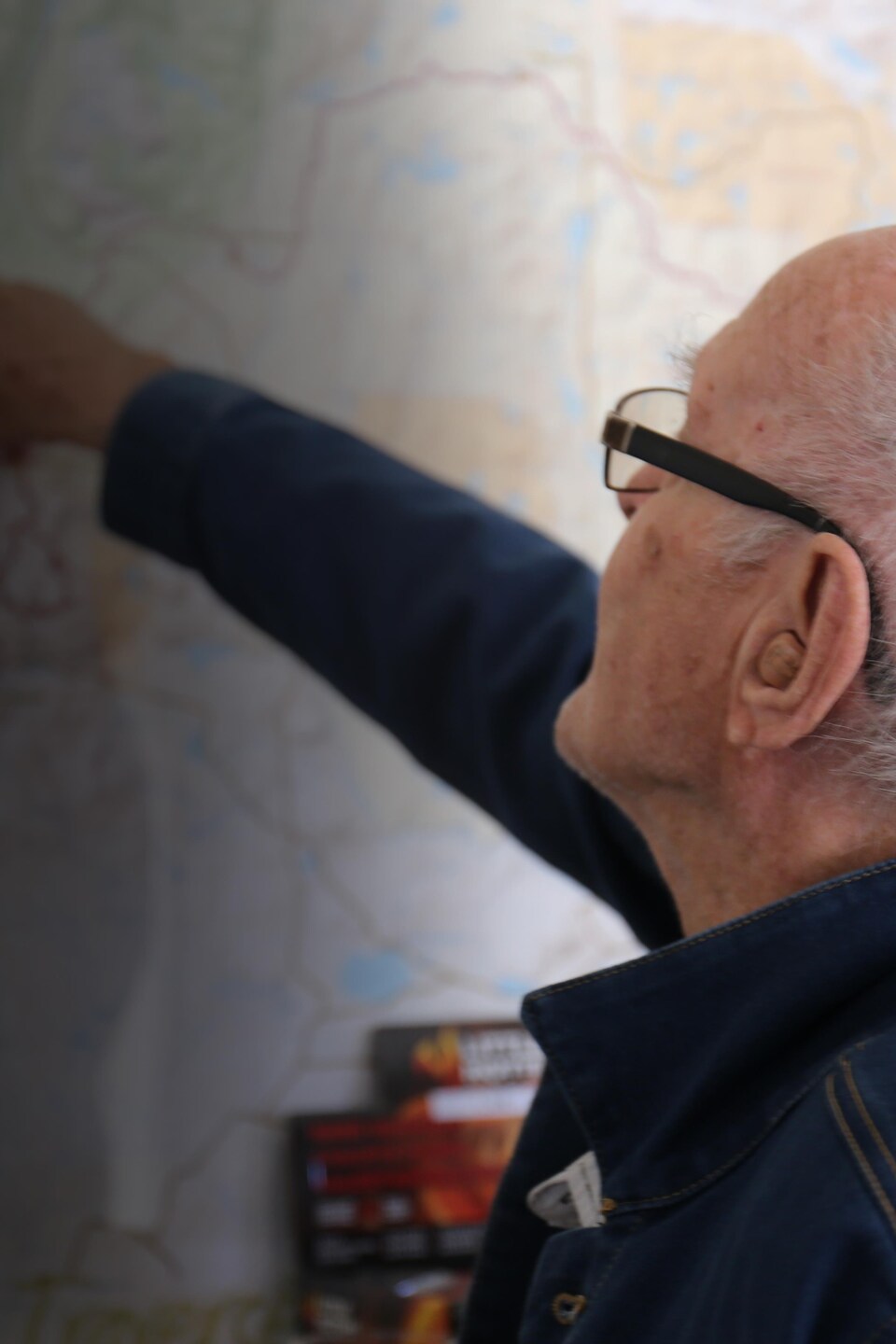 Un homme âgé pointe un endroit sur une carte posée au mur. 