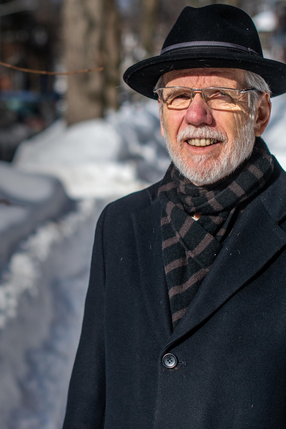 Un homme à la barbe blanche pose à l'extérieur devant un banc de neige. 