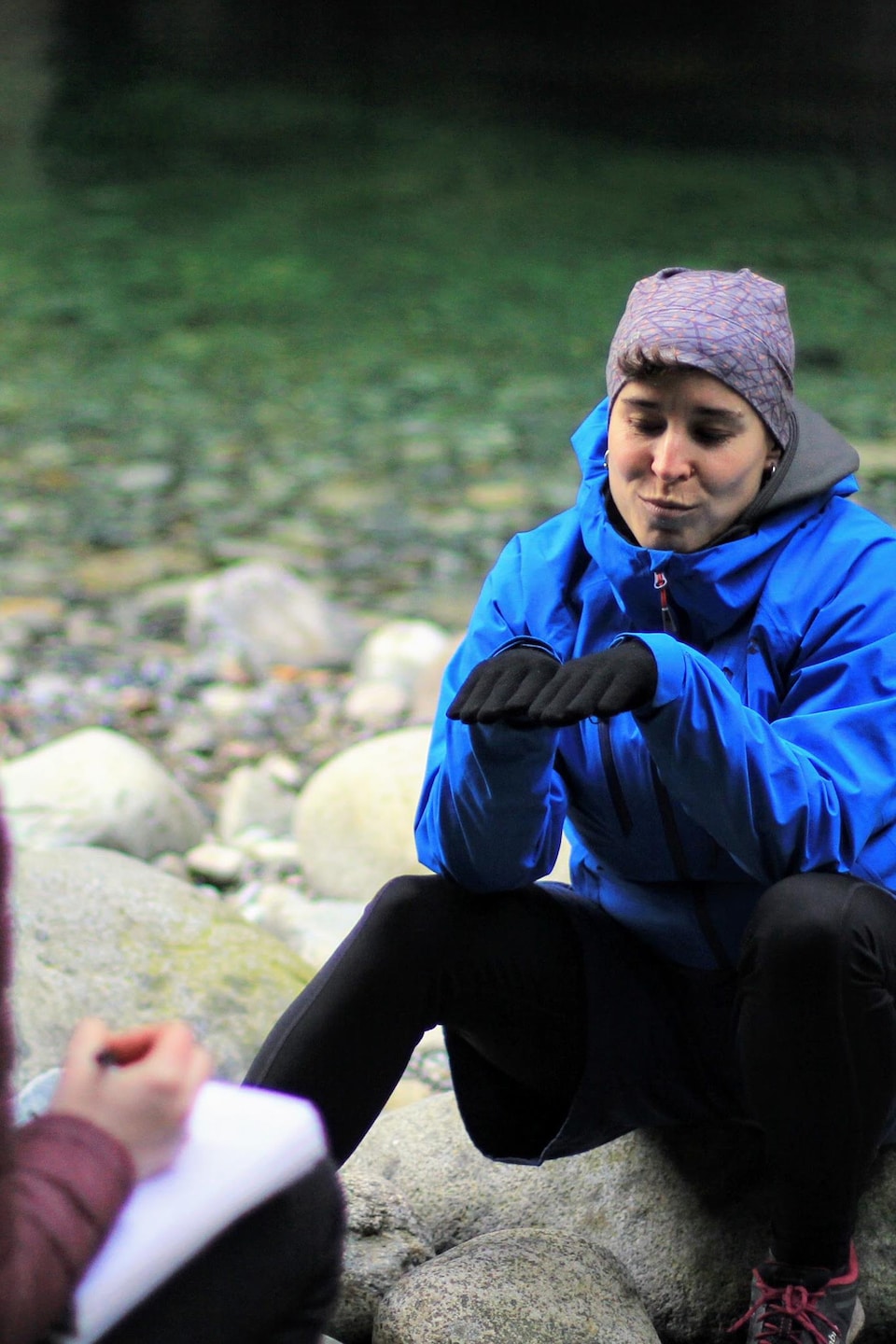 Mireille Langlois et Joëlle Perras en entretien, assis sur des rochers sur le bord de l'eau.