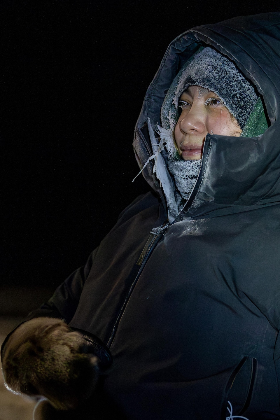 Une femme en habit hivernal avec du frimas pose de profil le soir.