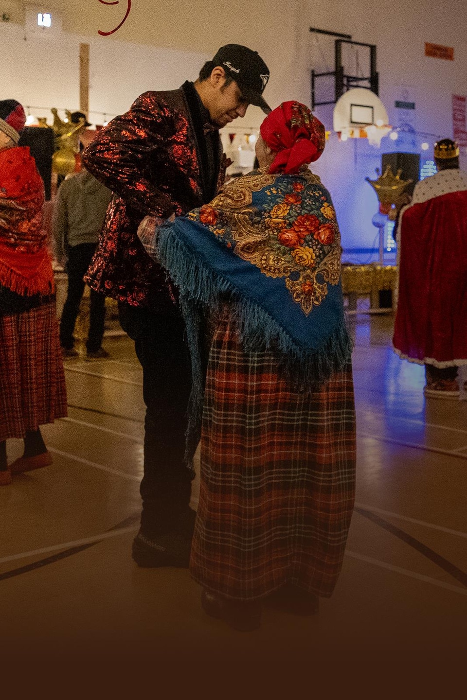 Des couples de plusieurs générations dansent dans un gymnase décoré pour une fête communautaire.
