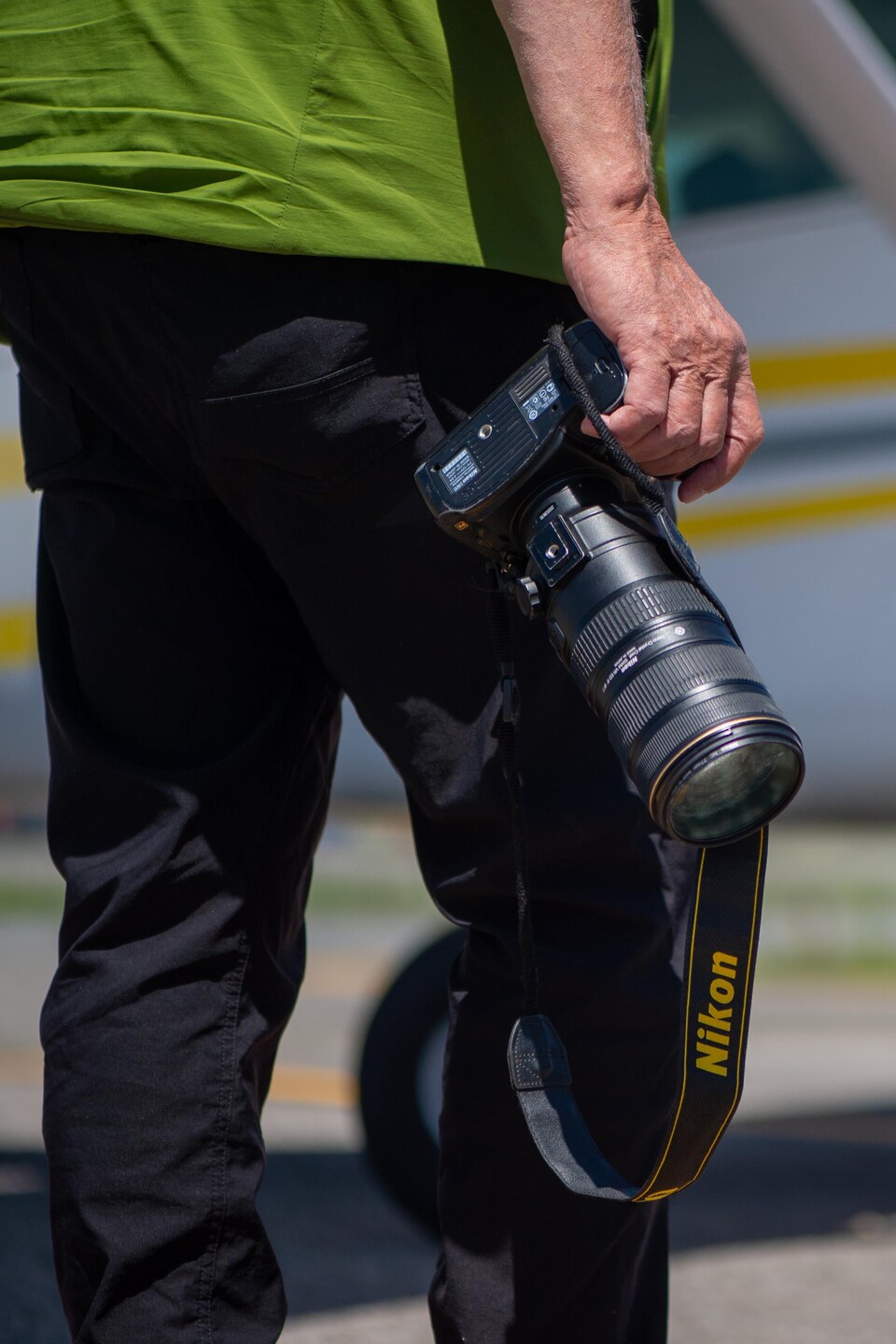 Un homme de dos avec un appareil photo devant un petit avion sur une piste. 