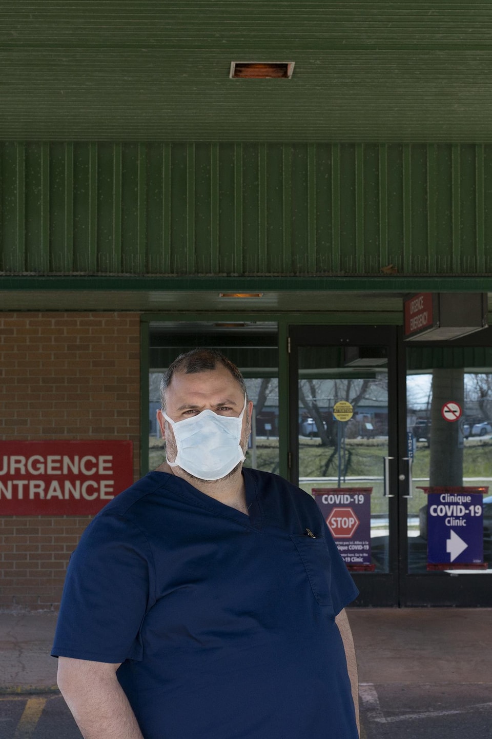 Un travailleur médical, debout devant une entrée d'urgence, porte un masque.