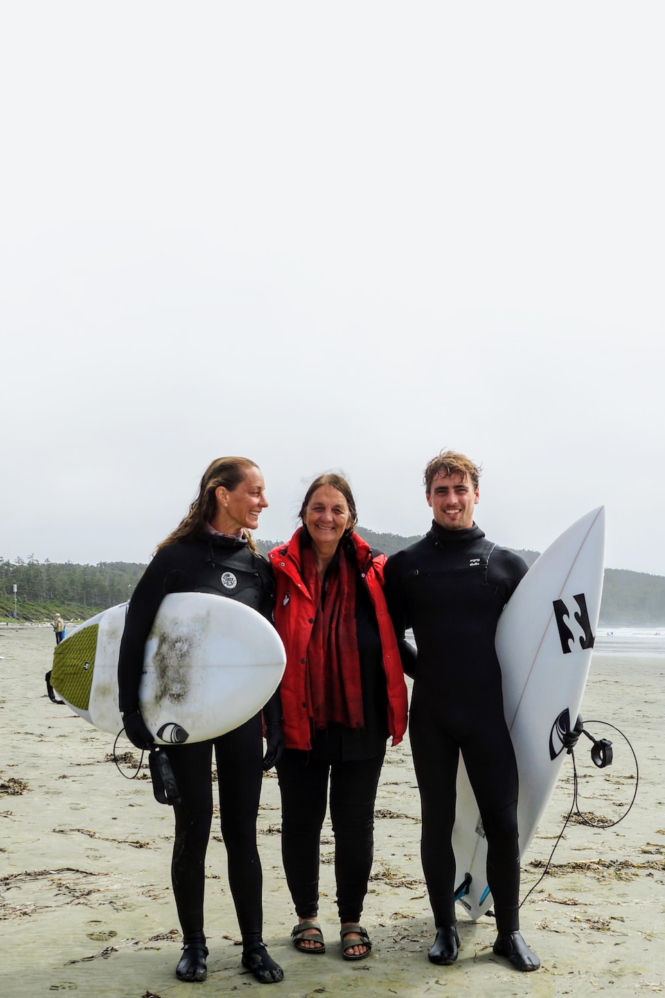 Deux surfeurs accompagnés d'une femme sur une plage.