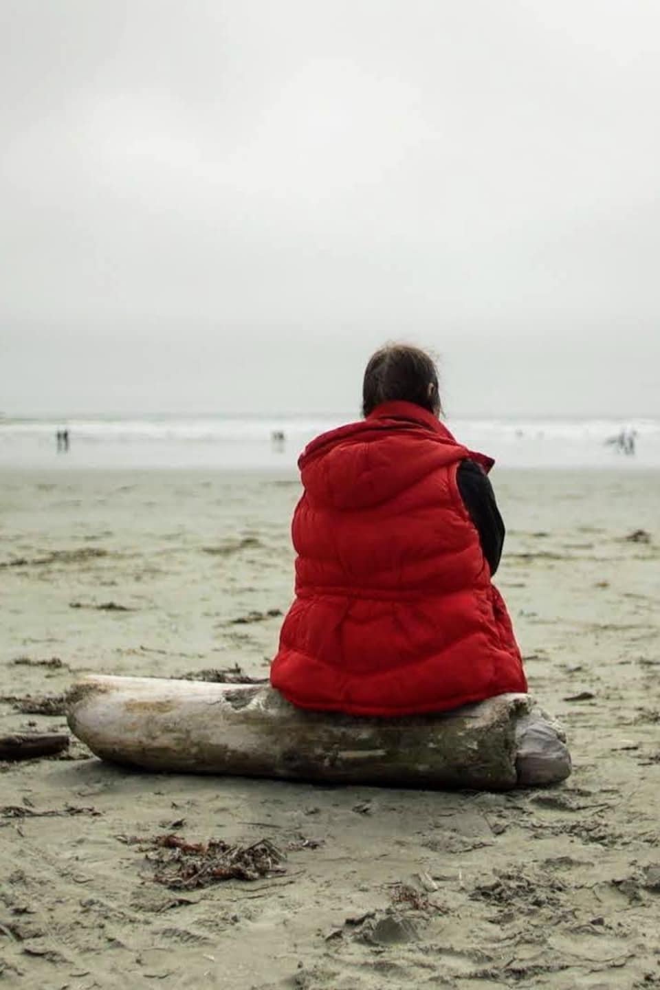 Gisèle assise sur un tronc mort sur la plage.